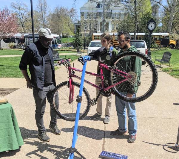 Two students look at a bike on a stand while a professor explains bicycle maintenance.