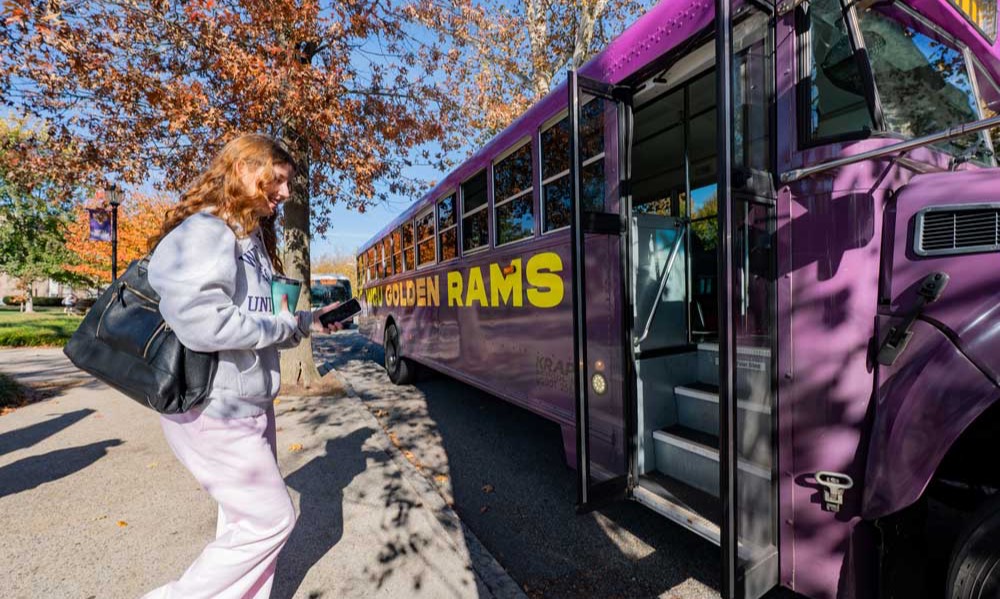 A student is walking onto WCU's purple branded Shuttle bus