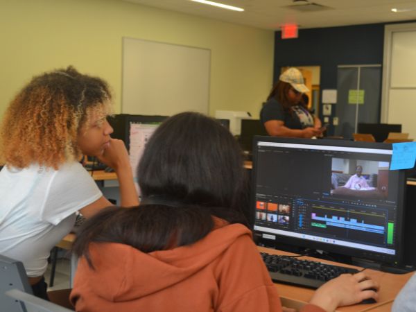 [Two students looking at a computer screen and editing a video project]