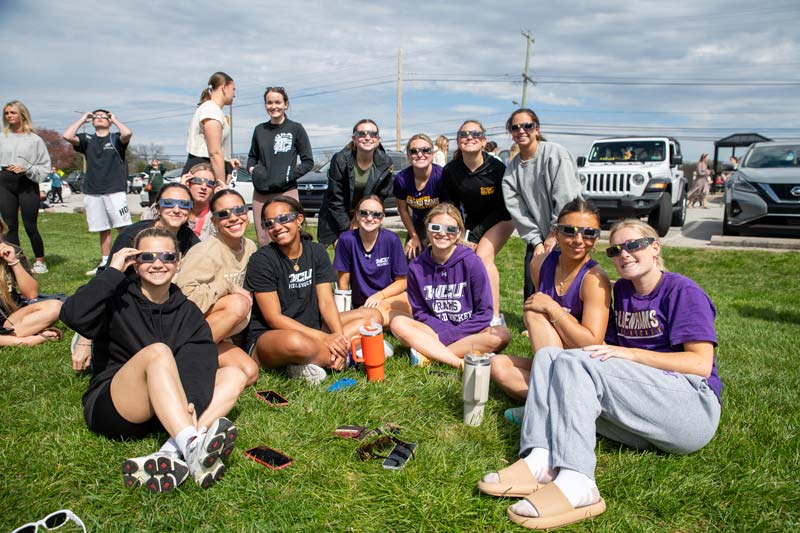 Students sitting on the grass wearing special sunglasses to watch the eclipse for an event held on WCU South Campus.